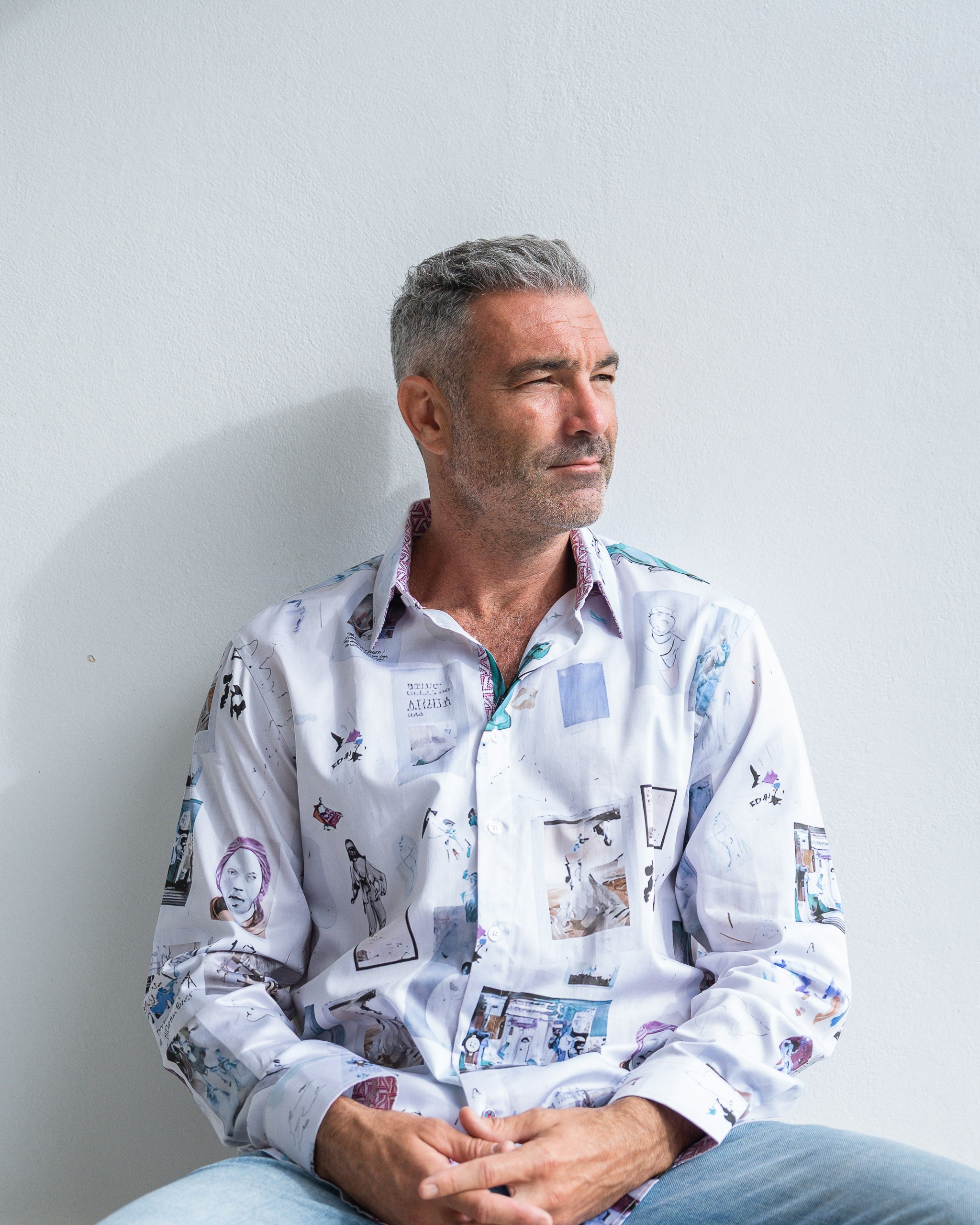 Man wearing a patterned shirt sitting against a plain background