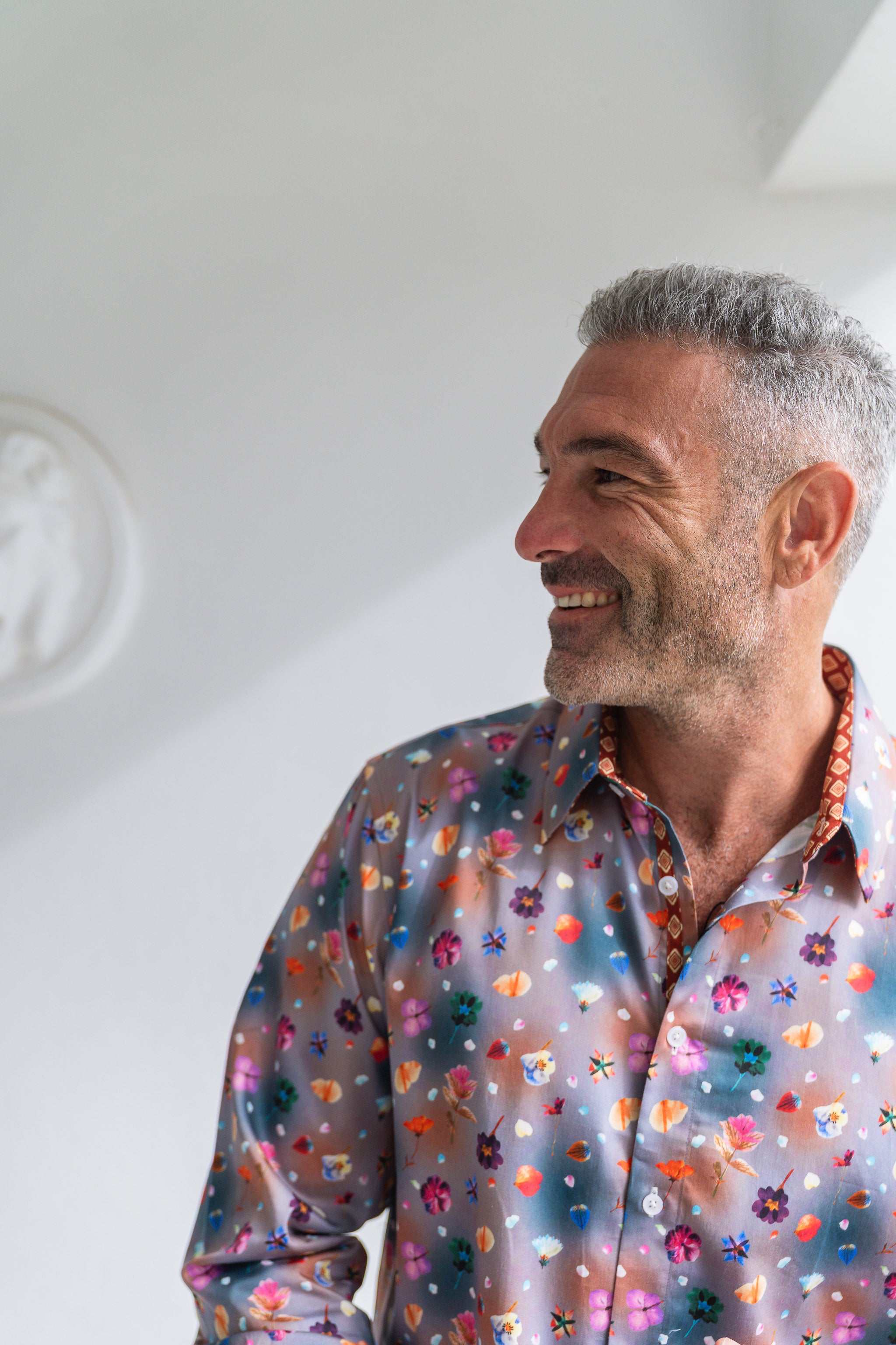 Man smiling, wearing a colourful floral shirt against a white wall