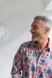 Man smiling, wearing a colourful floral shirt against a white wall