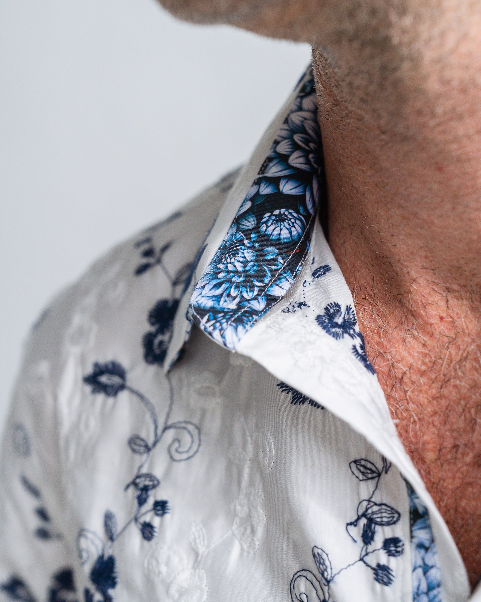 Close-up of a person wearing a white shirt with blue floral patterns on the collar and cuffs.