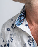 Close-up of a person wearing a white shirt with blue floral patterns on the collar and cuffs.