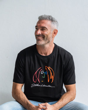 Man wearing a black t-shirt with colourful John Lennon motif, sitting against a light grey background