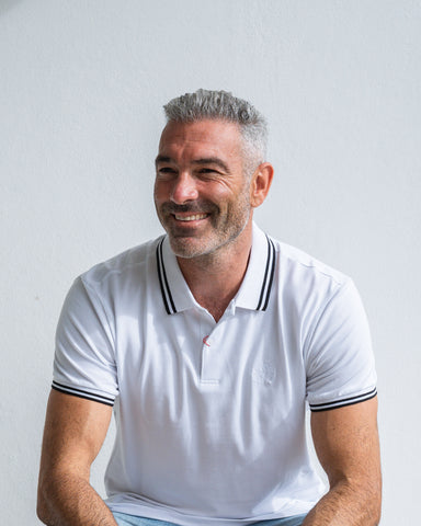 Man wearing a white polo shirt with black trim against a light gray background