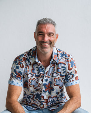 Man wearing a patterned shirt sitting against a plain background
