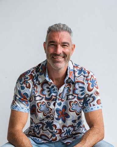 Man wearing a patterned shirt sitting against a plain background