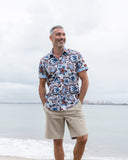 Man wearing a patterned shirt and ecru shorts standing on a beach.