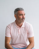 Man wearing a light pink polo shirt against a plain background