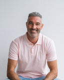 Man wearing a pale pink polo shirt against a plain background