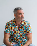 Man wearing a colorful geometric patterned shirt against a plain background