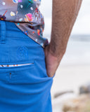 Man wearing blue shorts with a John Lennon logo, colourful shirt, and blurred background