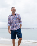 Man wearing a patterned shirt and navy shorts standing on a beach.