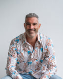 Man wearing a patterned shirt sitting against a plain background
