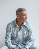 Man wearing a pink patterned shirt sitting against a plain background