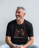 Man wearing a black t-shirt with colourful John Lennon motif, sitting against a light grey background