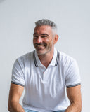 Man wearing a white polo shirt with black trim against a light gray background