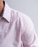 Close-up of a light pink shirt with floral embroidery on a gray background
