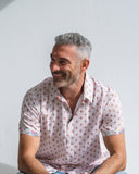 Man wearing a patterned short sleeve shirt sitting against a plain background