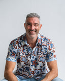 Man wearing a patterned shirt sitting against a plain background